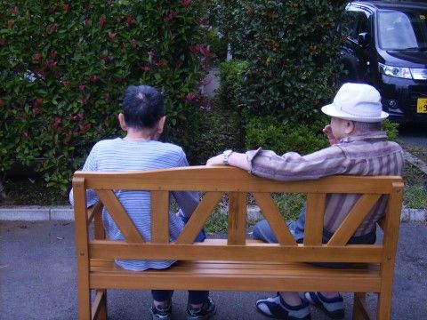 屋外に設置された木製のベンチに座っている、二名の男性入居者