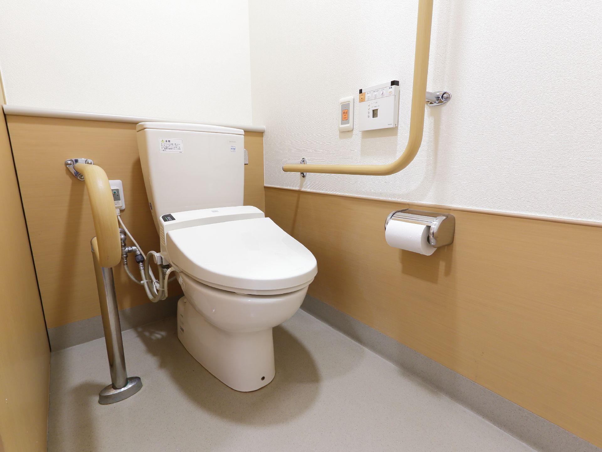 洋式トイレは、ウォシュレットタイプとなっている。壁には緊急時のブザーが設置してある。手すりが両サイドについている。