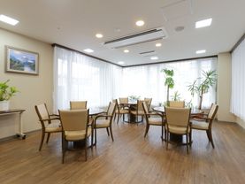 3つのラウンドテーブルと、それぞれに4脚ずつ椅子がセットされている。床は、バリアフリー。部屋の三面が窓になっているので、陽光が入りやすい。