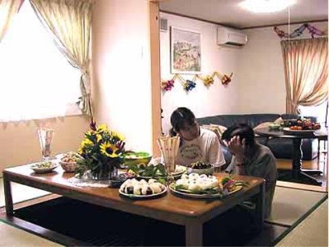 掘りごたつ式のテーブルの上に、ひまわりなどの花が飾られ、おむすびなどの料理が並べられている様子