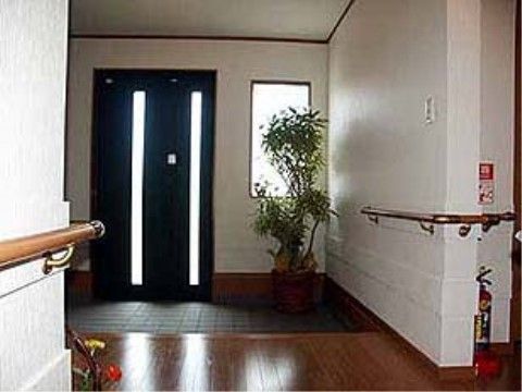 タイル敷きの玄関はゆったりとしていて広い。ドアの横にはグリーンが置かれている。玄関横の壁には手すりが取り付けられている。