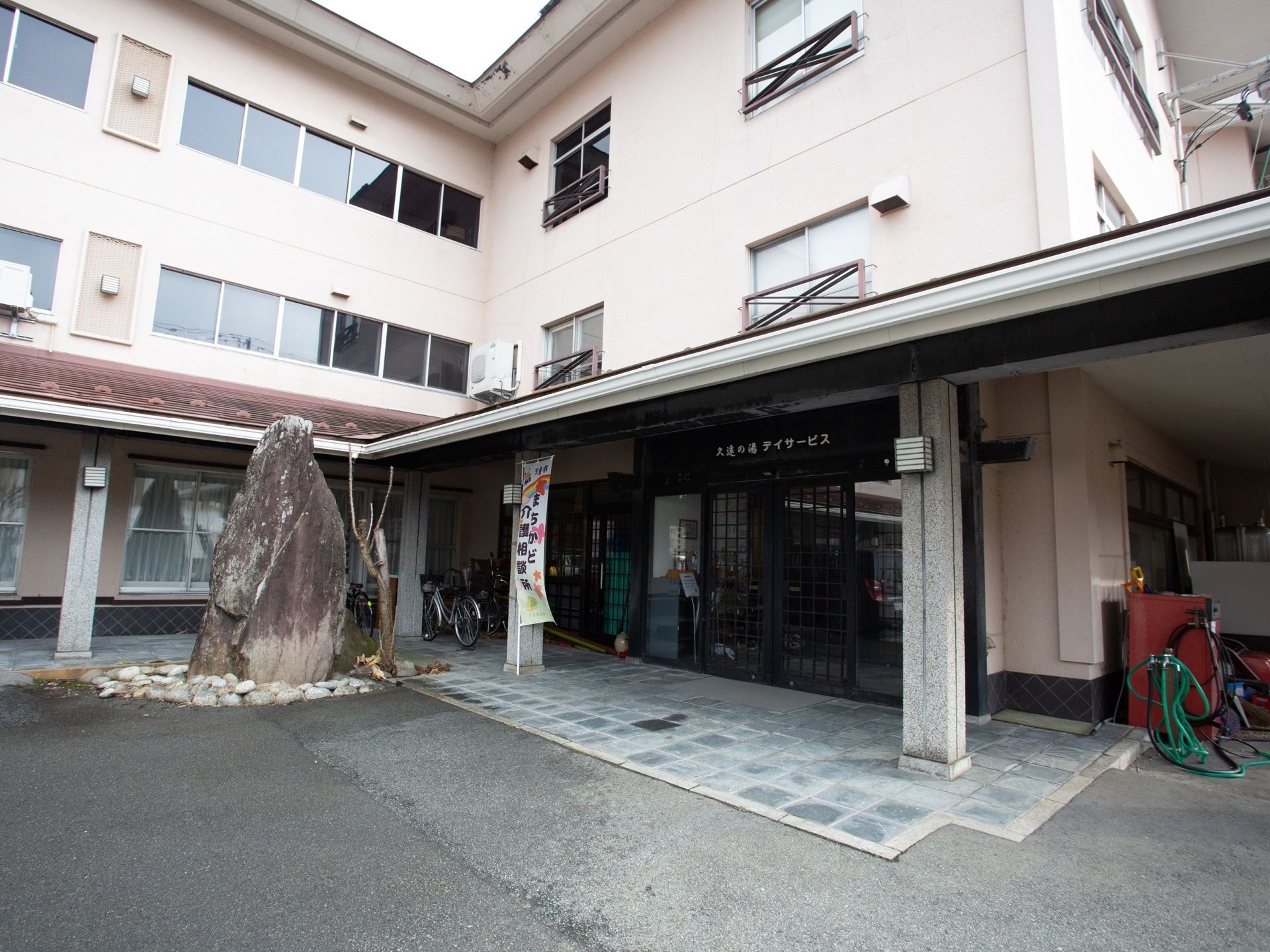 デイサービスの玄関である。屋根のある玄関の上部には、施設名が表記されている。玄関の右前には巨石が飾られている。
