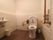手すり付きの洋式便器が設置されたトイレの近くには洗面台が設置されている。洗面台の下には白いゴミ箱が置かれている。