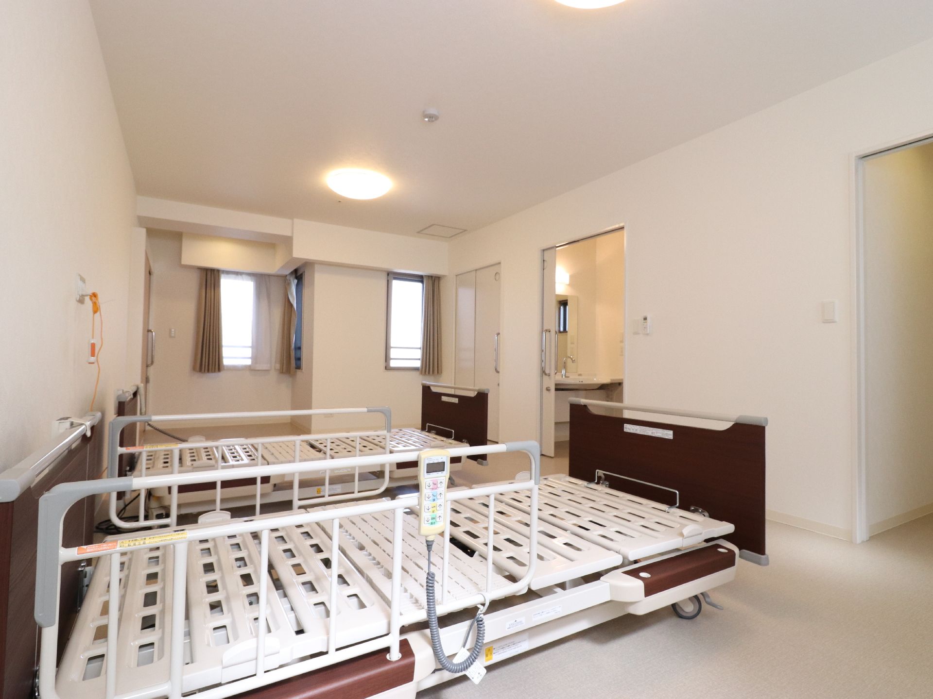 全体的に白でまとめられたデザインの二人部屋である。右奥には、明るい照明が付いた洗面台が設置されているのが見える。