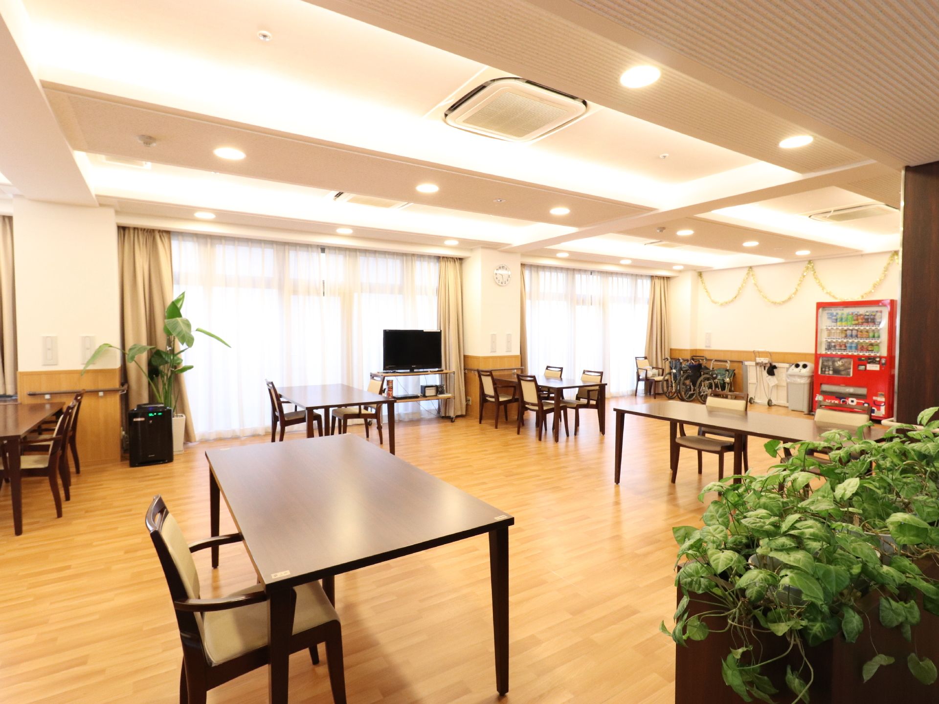 フローリングのへやに部屋に大きな窓がある。テーブルと椅子がスペースを空けてゆったりと置いてあるので車。椅子でも間を通り易い。
