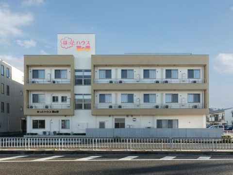 敷地の周囲はフェンスで囲まれている。横に長い長方形の建物があり、たくさんの窓とエアコンの室外機が見える。