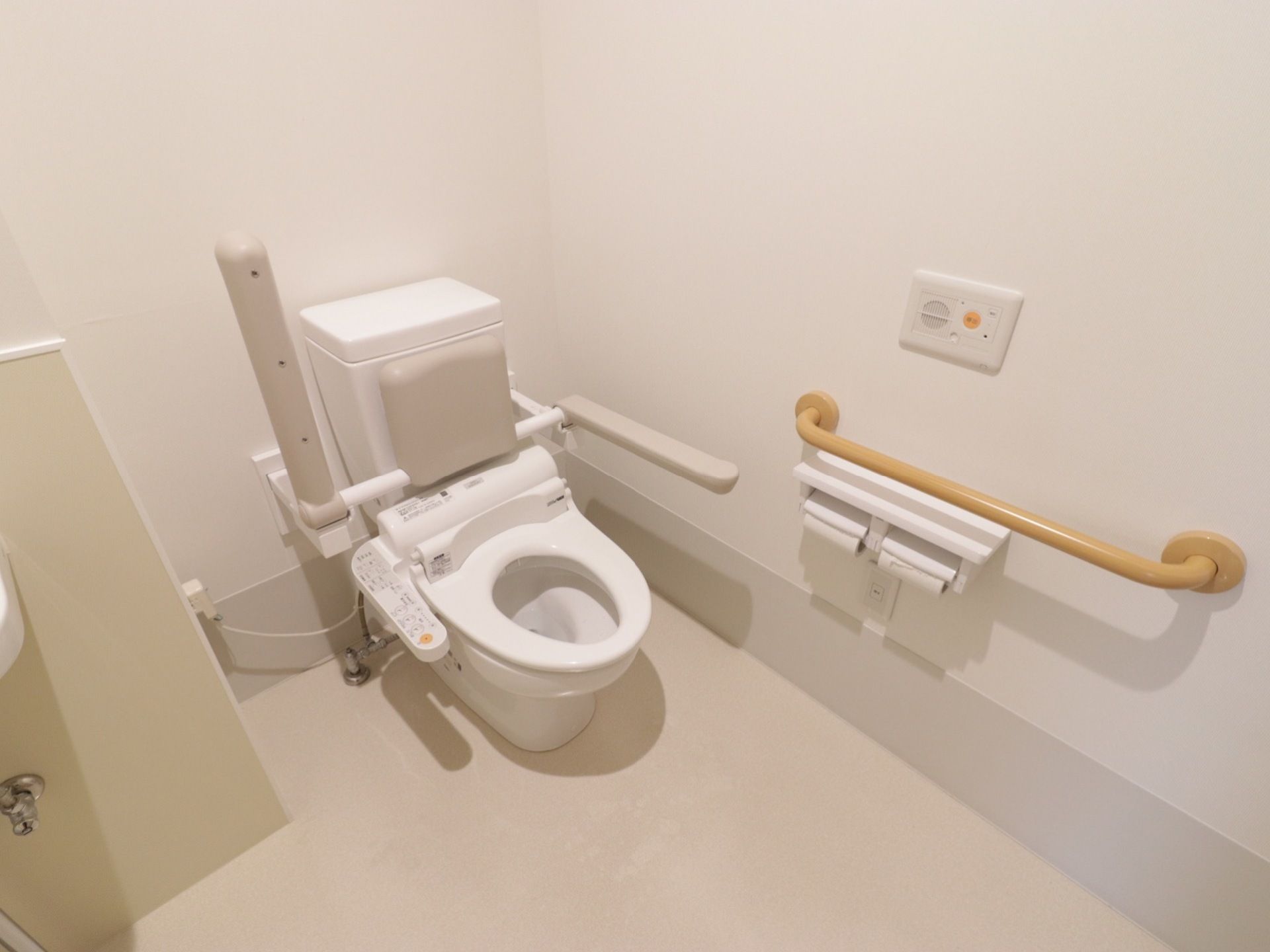 トイレは洋式である。便器の両側に可動式の手すりが取り付けられている。タンクには背もたれが付いている。