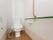 白いウオッシュレットトイレの左手にはナースコールがついている。右手には緑と茶色の手すりが設置されている。