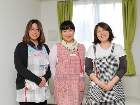 窓の前に立ち、笑顔を見せているエプロン姿の女性スタッフ三名