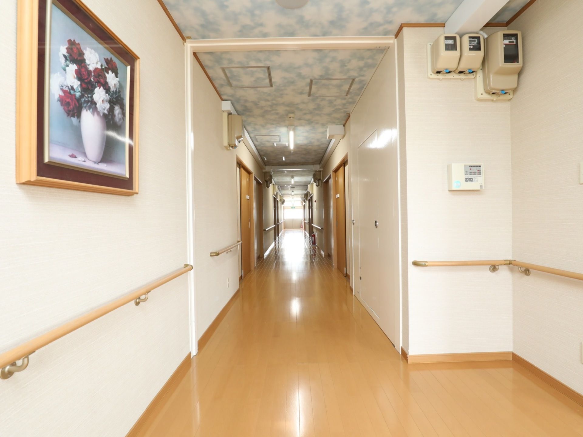 明るい床色、白い壁でコーディネートされた通路である。天井は雲をイメージしたデザイン。壁には絵画が飾られている。