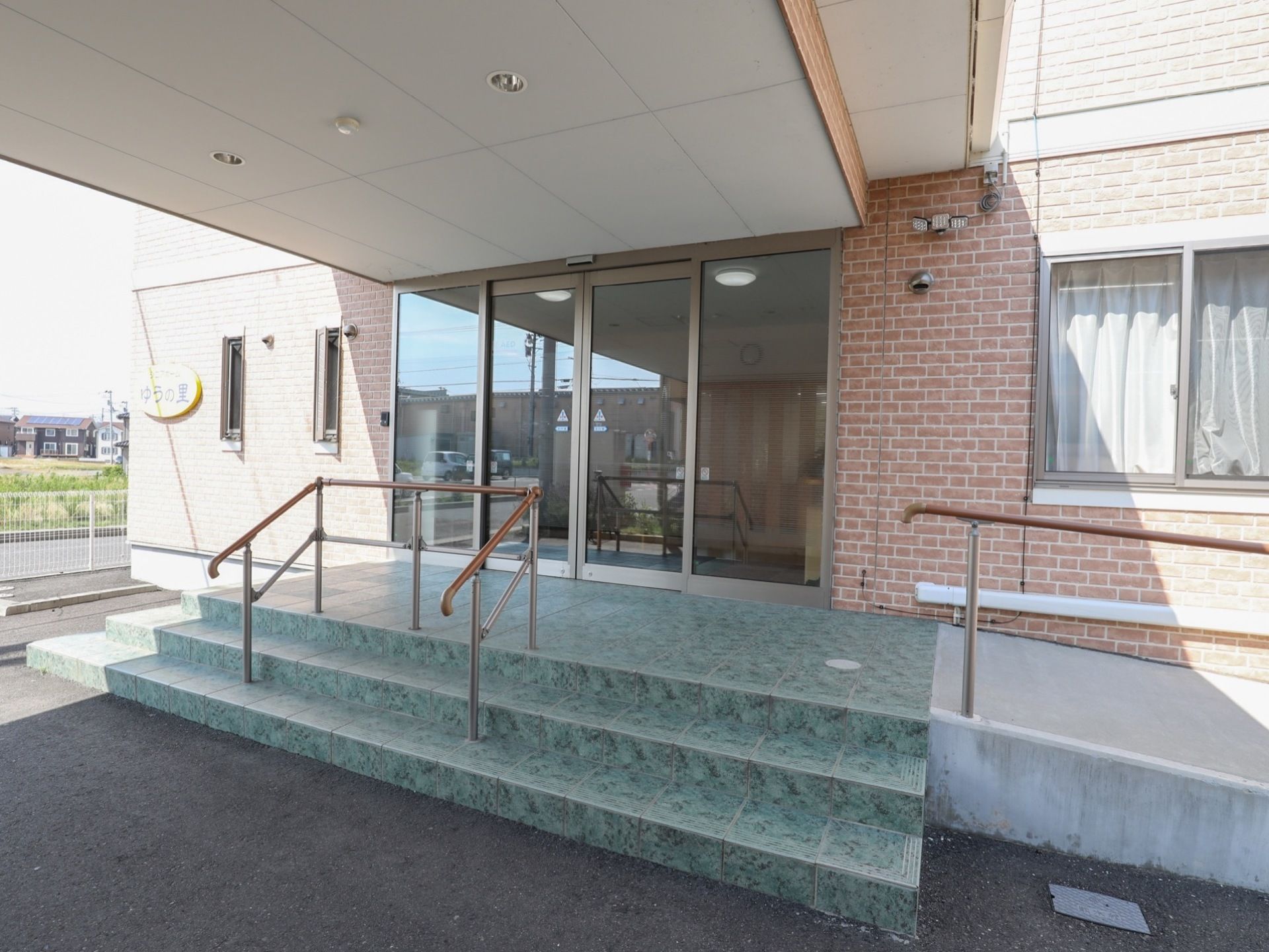 玄関にはガラス張りの自動ドアが設置されており、正面には3段の階段、右側にはスロープが設けられている。