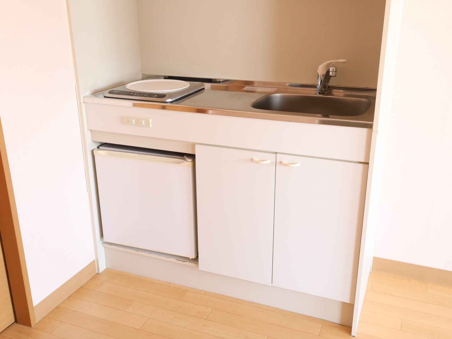 居室の一角には、白を基調としたキッチンが完備されている。シンクの下には、両開きの扉が取りつけられた収納スペースがある。