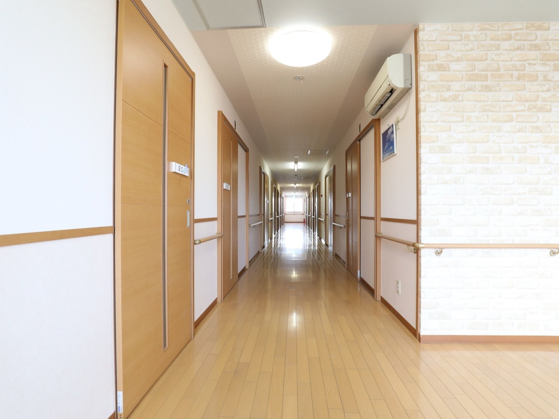 広々とした明るい廊下には、LEDライトとエアコン、手すりが完備されている。つきあたりには窓があり日射しが射し込んでいる。
