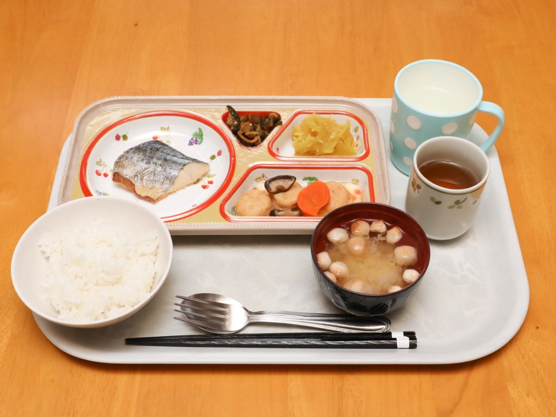 鯖、漬物、栗きんとん、筑前煮がプレートに盛られている。白米と味噌汁、湯飲みに入ったお茶と取っ手付きのコップに水が用意されている。
