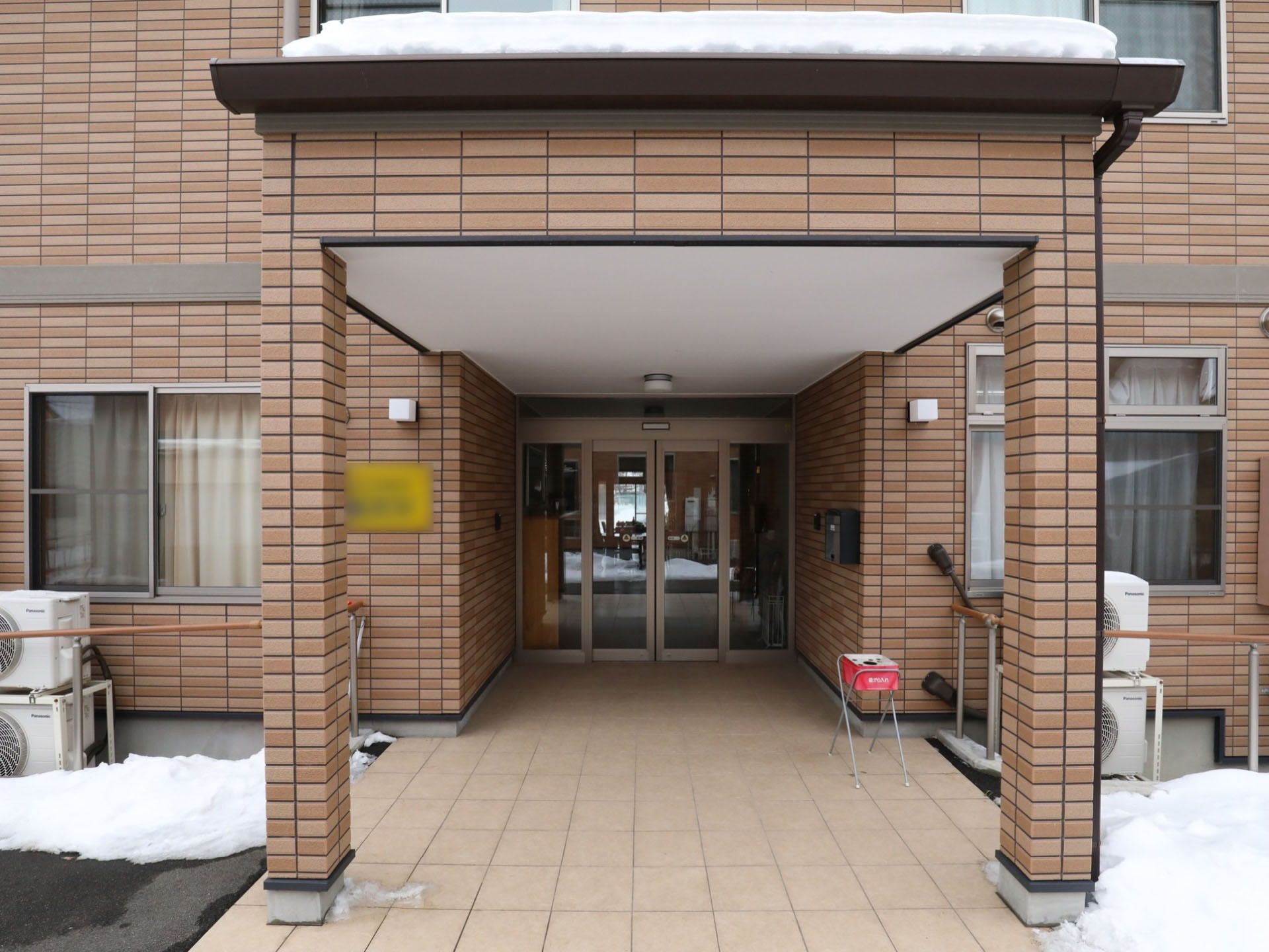 茶色のあたたかみのある建物。自動ドアの出入口までは足腰の不自由な方のため、手すりが備えられている。道には雪が積もっている。