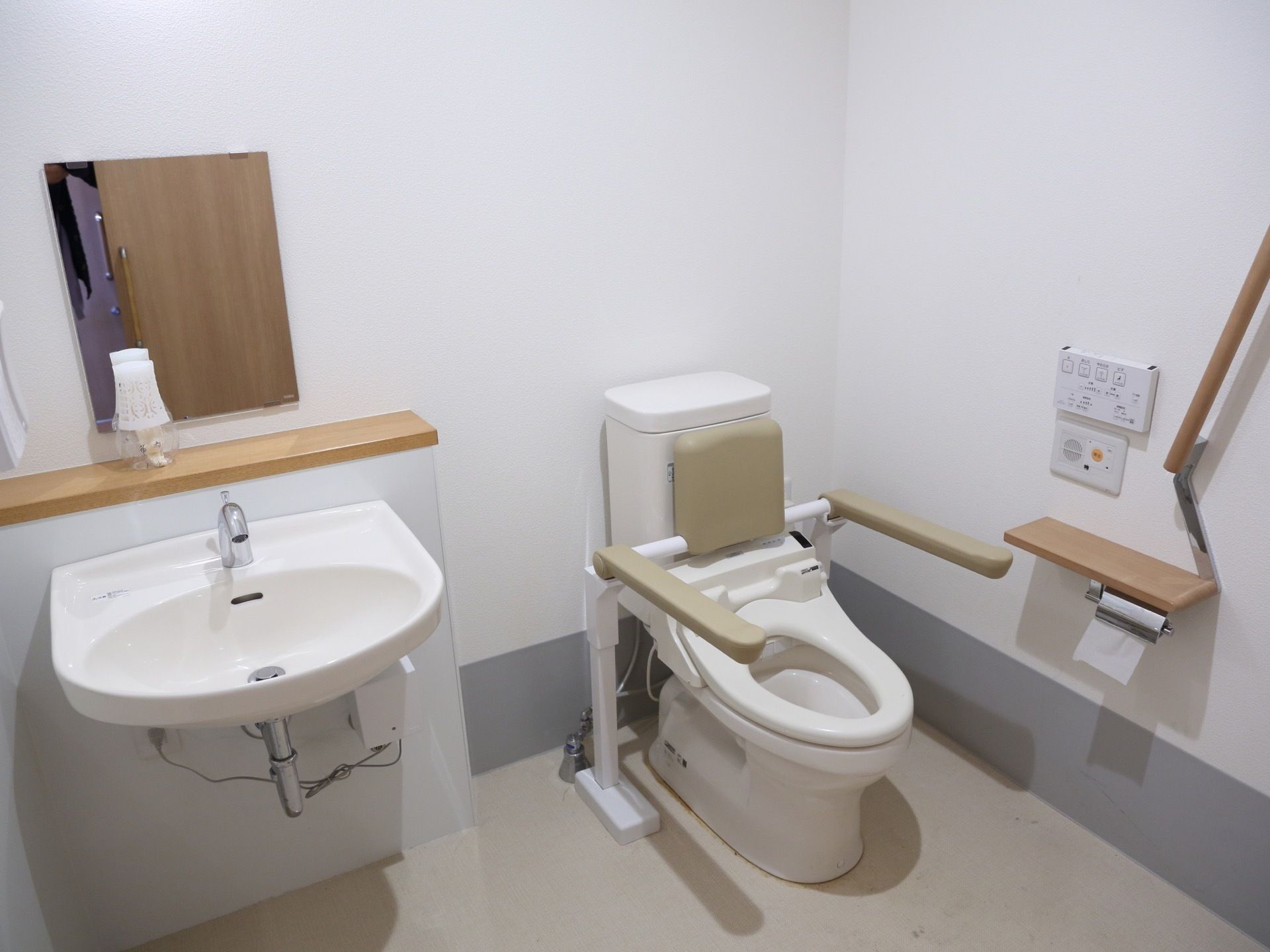 洋式便器が一据ある。便器のすぐ横に手洗い場が設けられている。温水洗浄便座が設置してある。リモコンの下に呼出ボタンが設置してある。