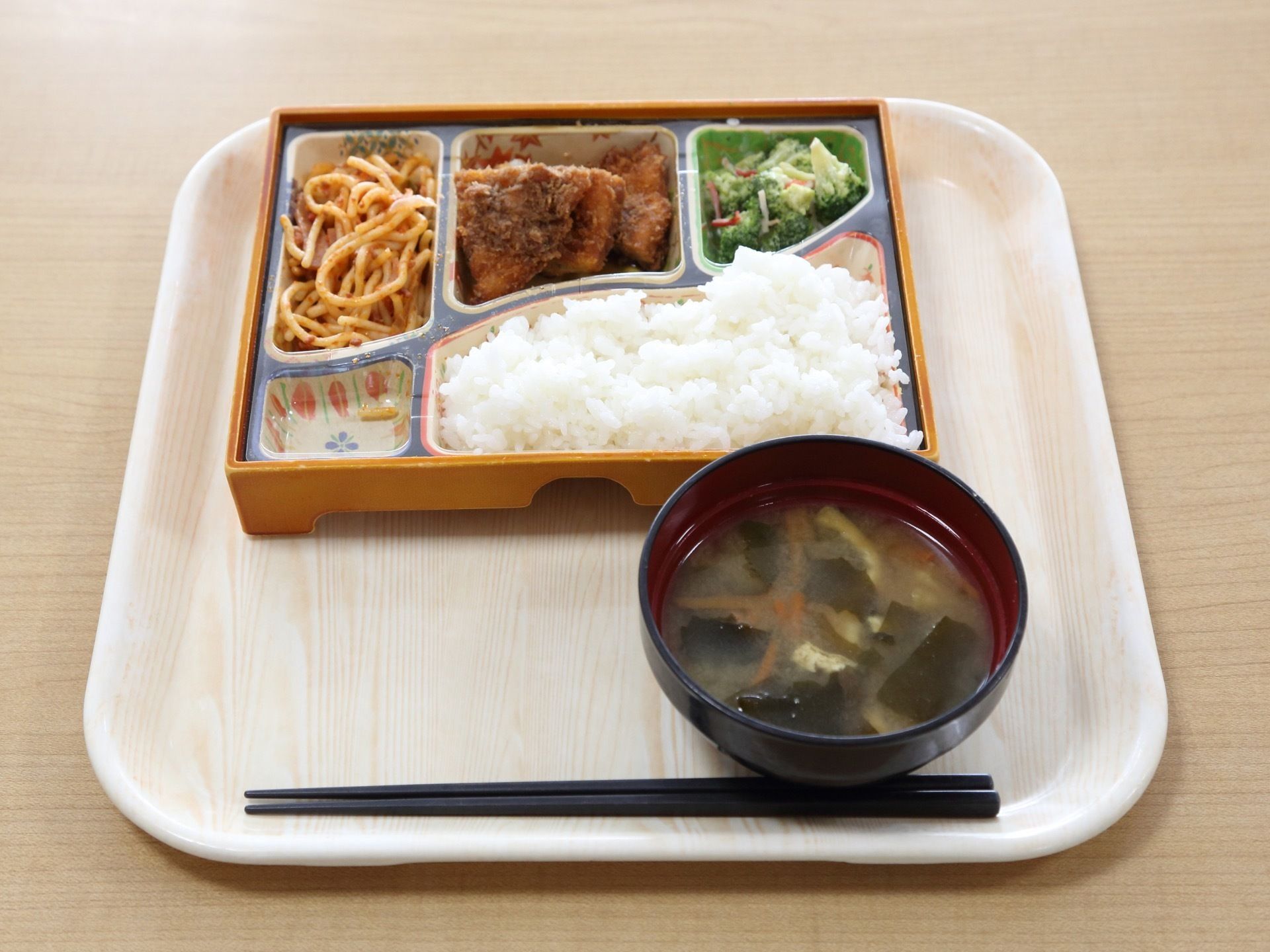 お盆の上にワンプレートの食器で食事が用意されている。味噌汁も用意されている。黒い箸が箸先を左に向けて置かれている。