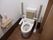 洋式トイレにはクッションの背もたれ、上から引き下ろすタイプの手すりが備わっている。左には呼び出しボタンが設置されている。