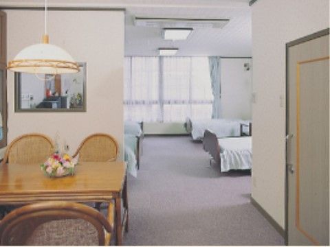 手前右側にはドアがある。隣には上から照明が下がり、テーブルを囲んで４脚椅子ある。奥は突き当りに窓があり、ベッドが左右に２台づつ並んでいる。
