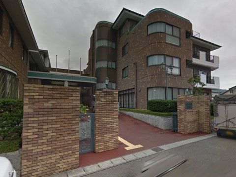 建物の外壁と同じ茶系のタイル張りの門柱があり、間は舗装されて奥へと続いている。歩道には点字ブロックもある。