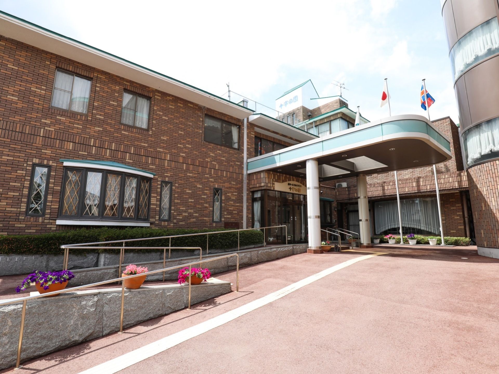 施設はレンガ調の外観になっており、入口付近には大きな屋根が設置されている。敷地内は広々としており、スロープが設置されている。