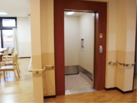 リビングの横に茶色の扉のエレベーターが１基設置されている。付近の壁には、手すりが取り付けられている。