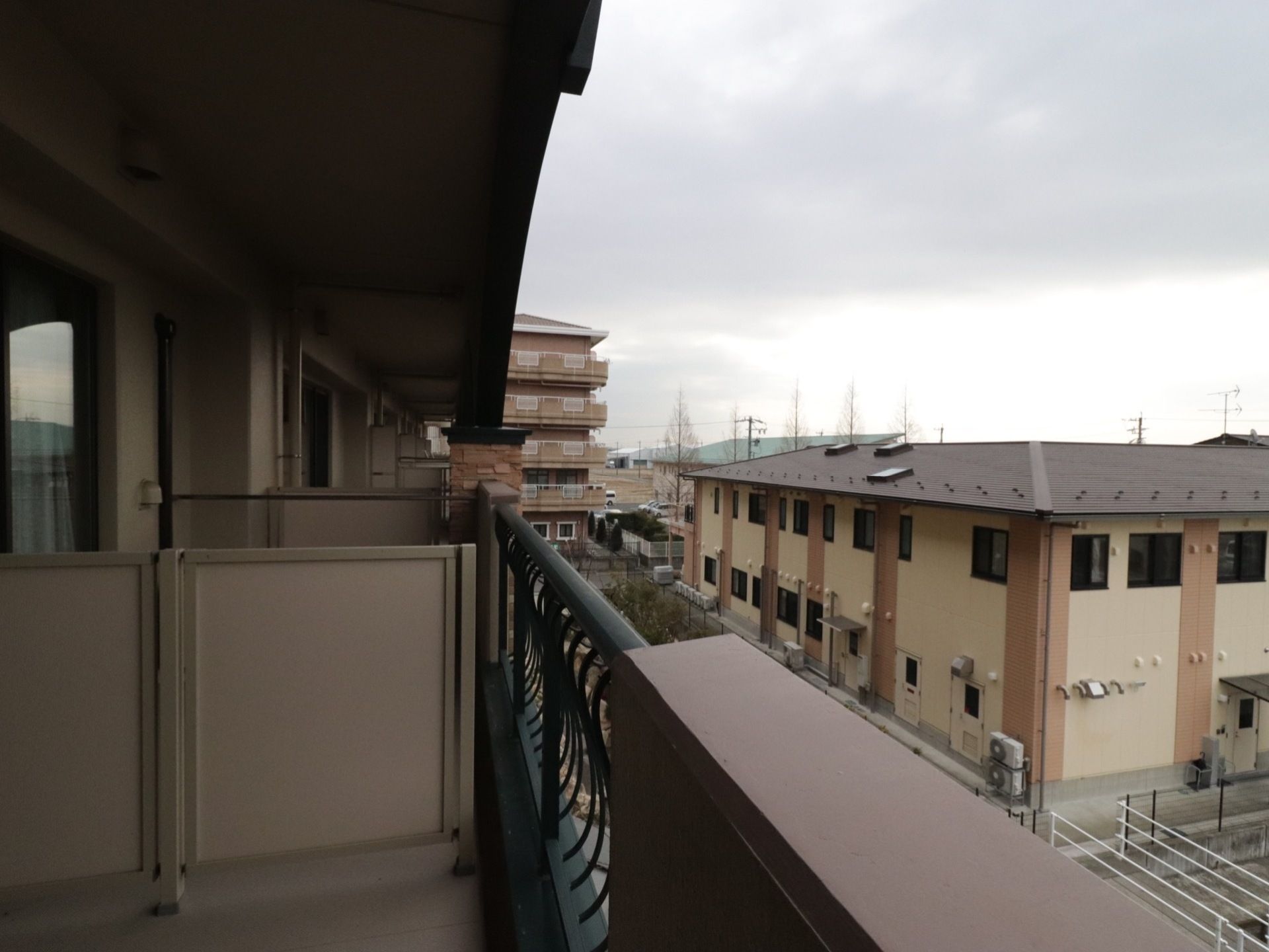 ベランダから近隣の建物が見えている。下の木々も見下ろすことができる。整備された比較的新しい建物が多い。