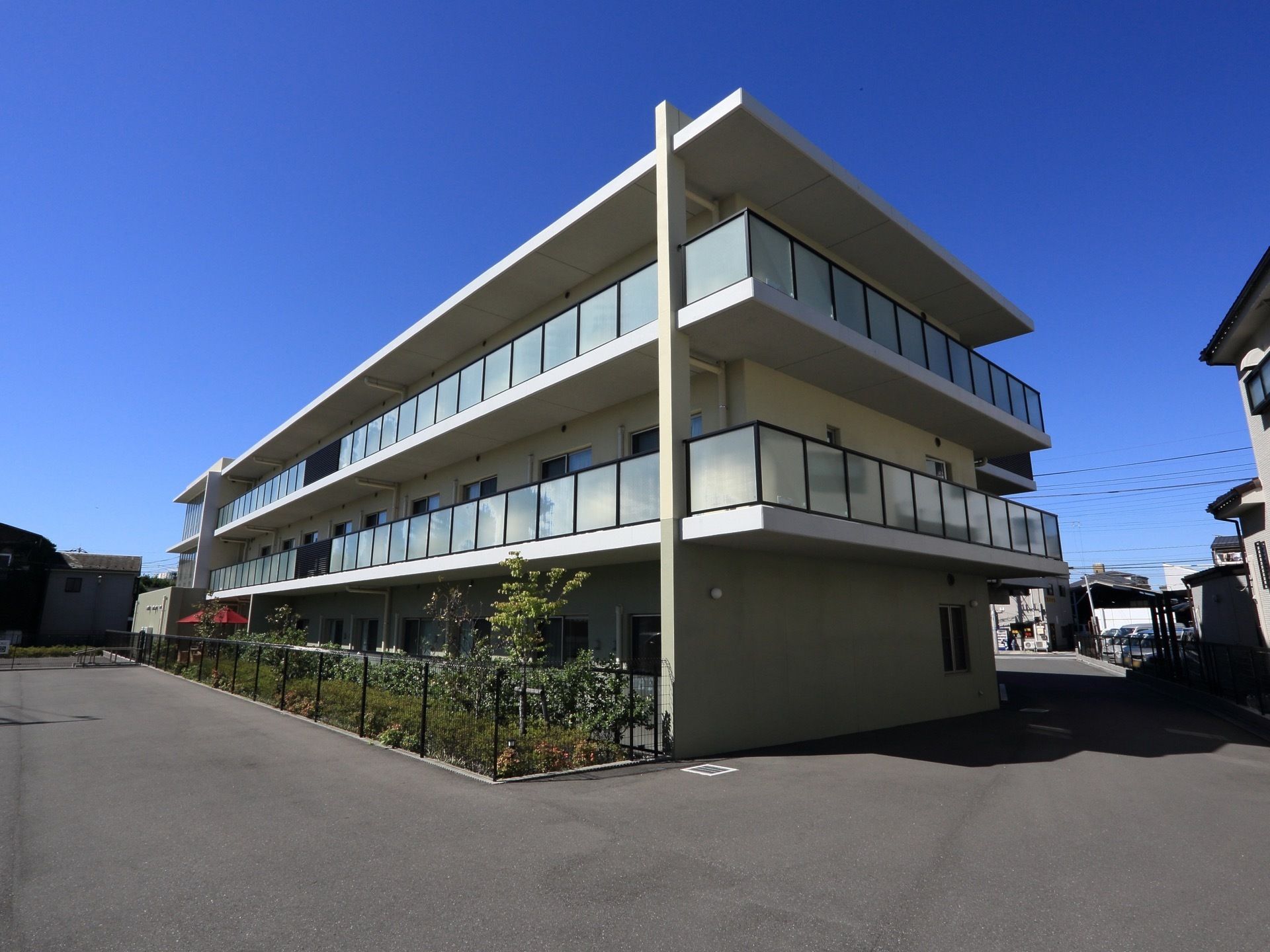 施設の建物は地上３階建てで、各階にはベランダが設置されている。建物の前には植え込みがあり、周囲は広々としている。
