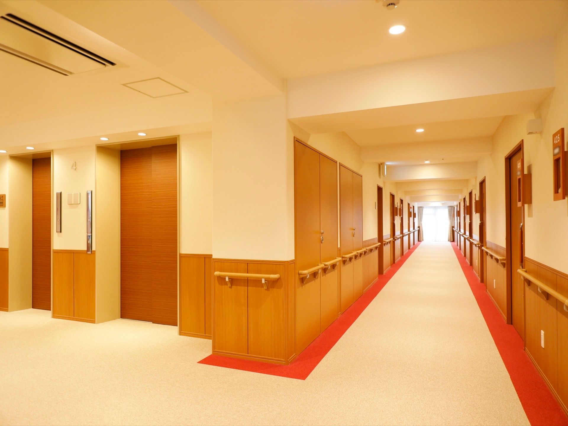 ブラウン系の色でまとめられた落ち着いたデザインの通路である。左端には、エレベーターが２基並んでいる。