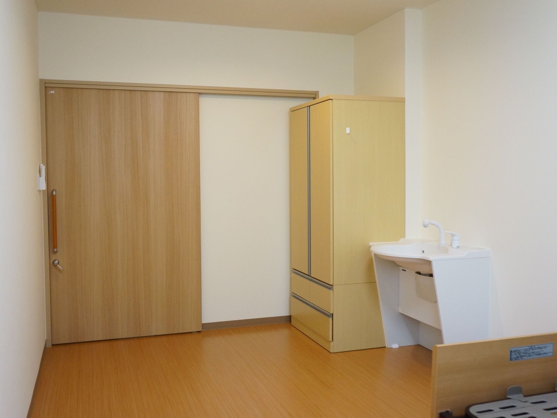 ドアは大きな木目調のスライド式になっている。室内には洗面台やベッド、クローゼットが備えてある。木の素材を多く使用したあたたかみのある空間である。