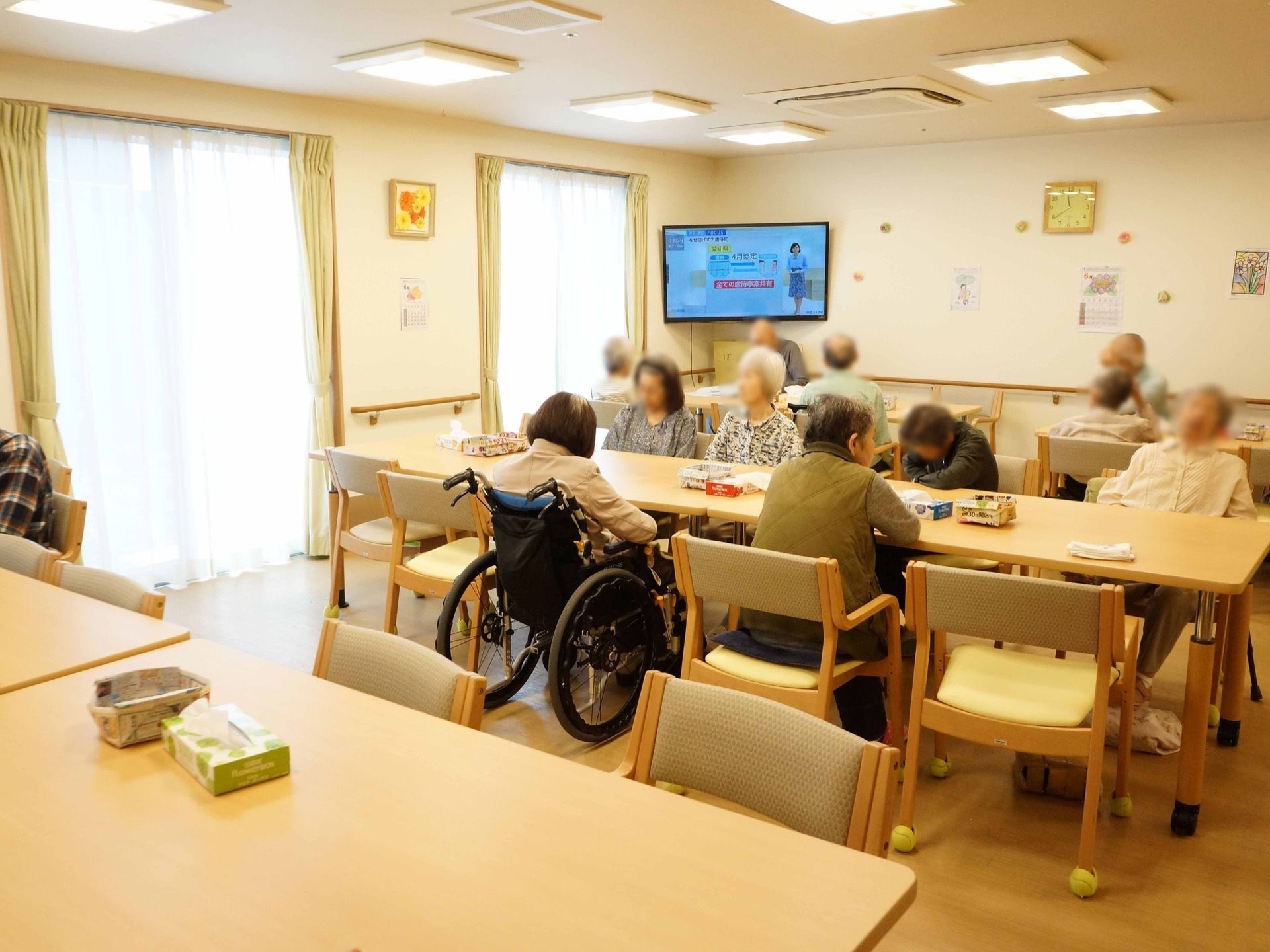 テーブルや椅子がたくさん並べられ、入居者様が座っている。椅子をどけると、車椅子をご利用の方もそのまま席に着くことができる。