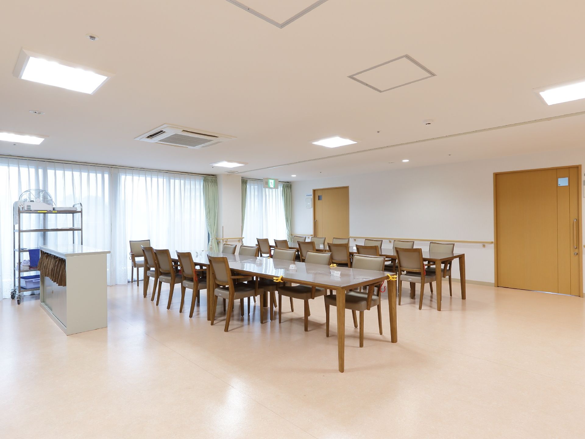 食堂を撮影した画像である。天井には四角い照明が設置されており、室内を照らしている。食堂の引き戸は木製で、画像右側の壁に2か所設けられている。