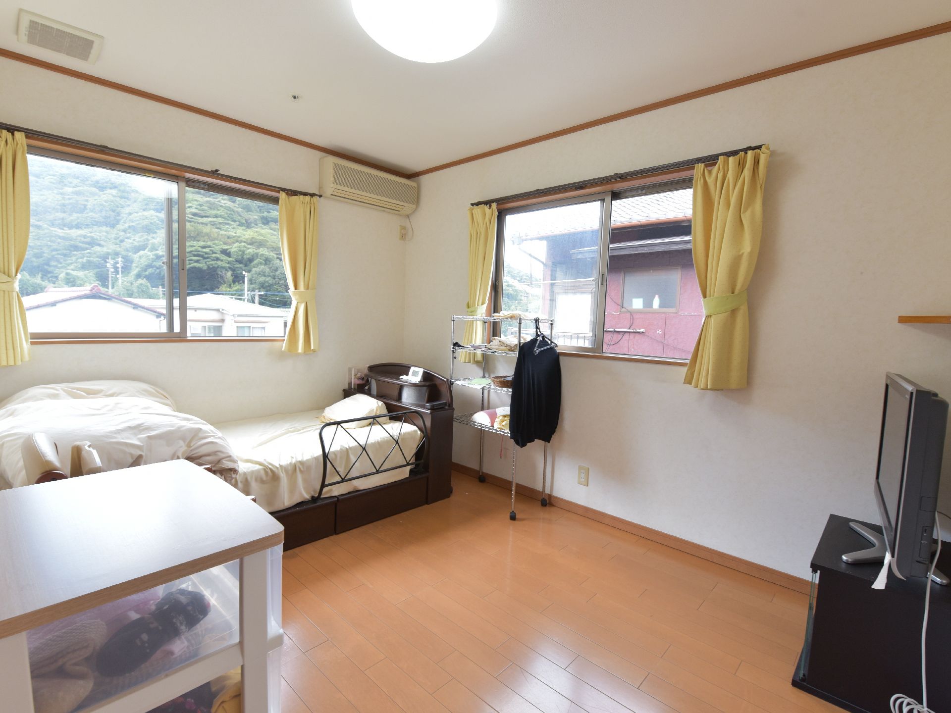 ベッドやテレビ、スチールラックなどが置かれている角部屋