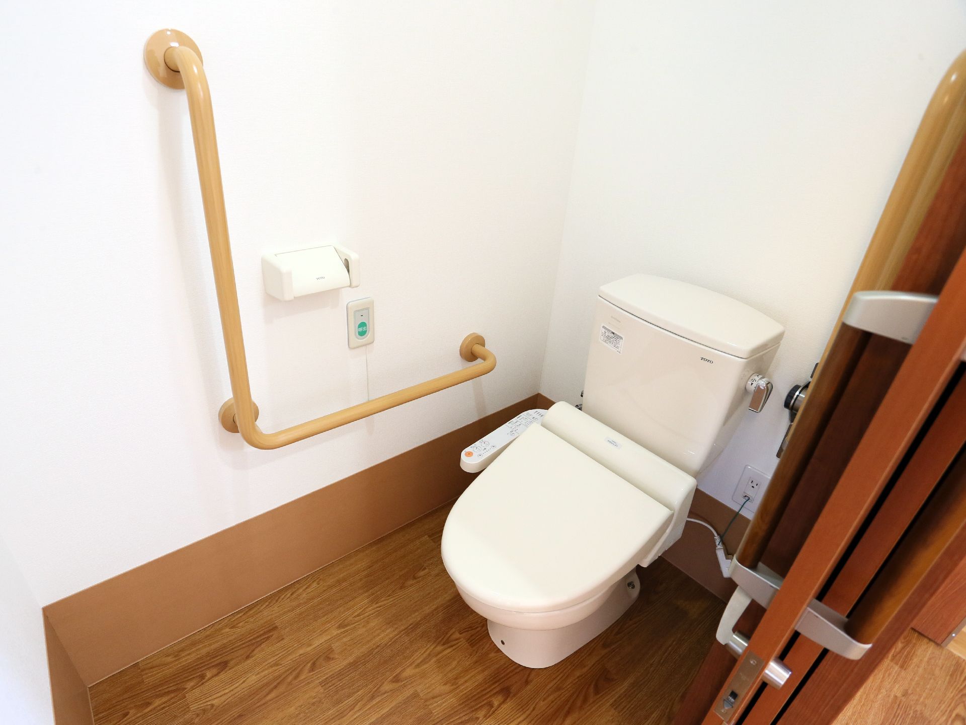ウォシュレット付水洗トイレである。立ったり座ったりを支える手すりが付いている。壁に緊急呼び出しボタンが取り付けてある。