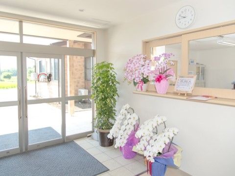 エントランスに大きな玄関マットが敷かれている。スタッフルームには花や植物が飾られ、明るい雰囲気。壁には時計がある。
