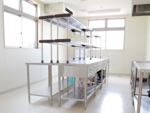 厨房は白を基調とした空間である。窓からは自然光が入り、明るい。作業台やラックは整理整頓されており、清潔感がある。