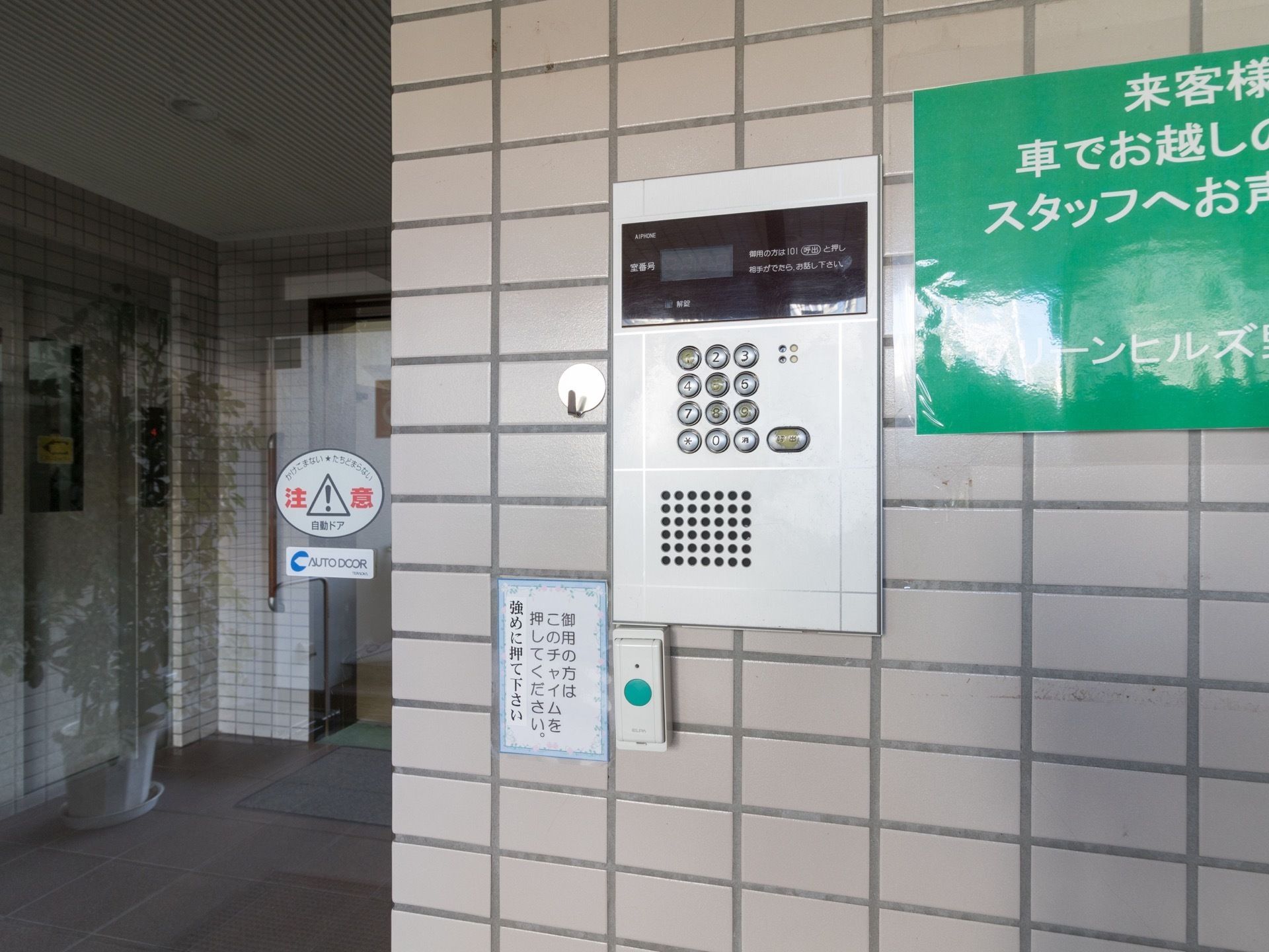 ベージュのレンガ調になった壁に、オートロックのインターホンとチャイムが設置されている。横には自動ドアがある。