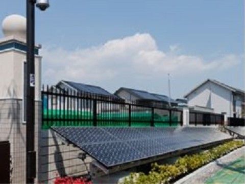 フェンスに沿うように太陽光発電のパネルが設置されている。パネルの下には植木があり、真上には青い空が広がっている。