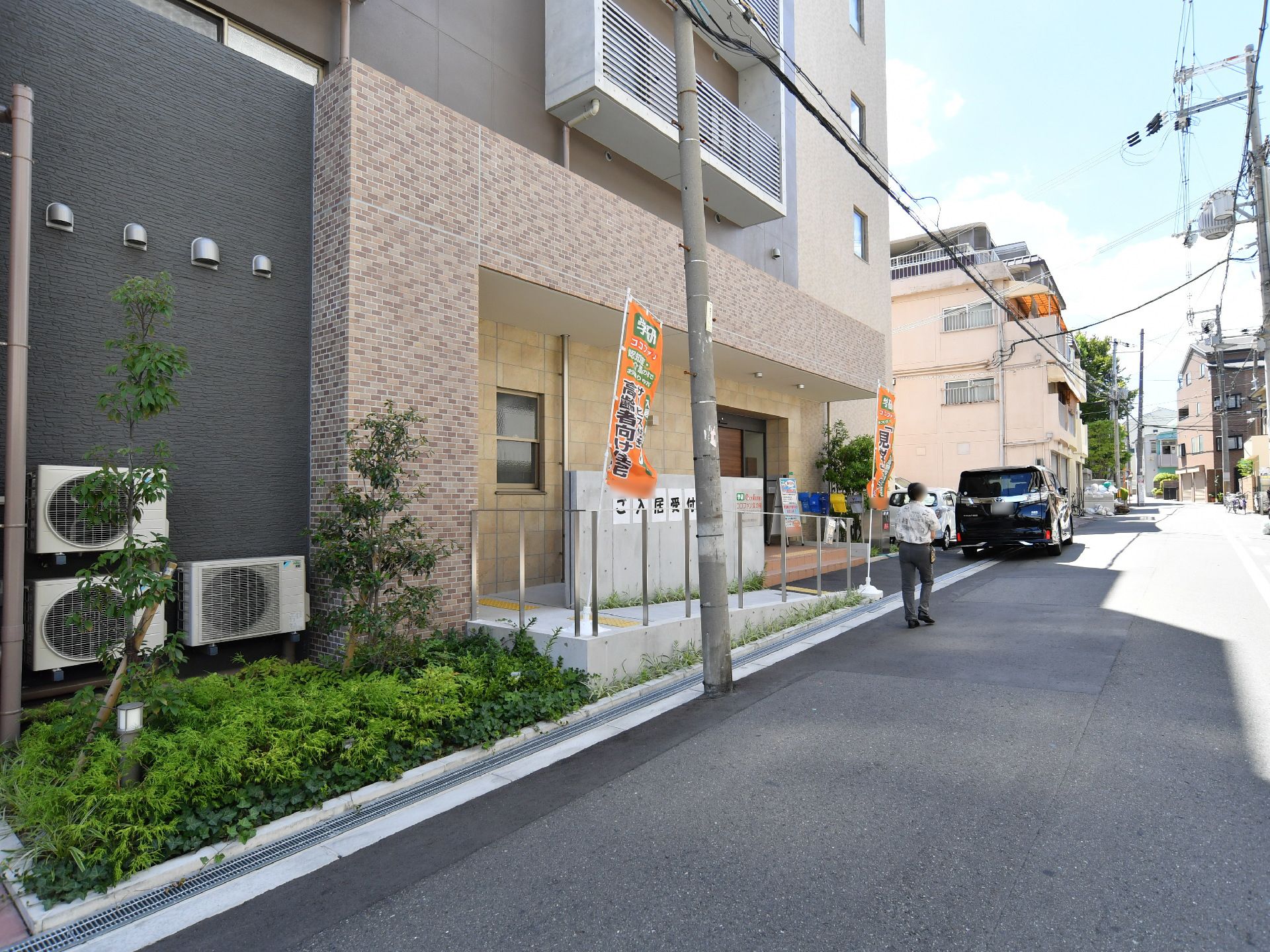 正面には電柱がある。その後ろにはスロープがあり、そこの右側には玄関がある。玄関の前には階段も付いている。