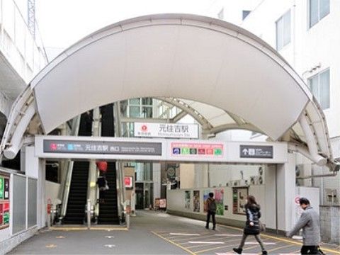 駅入口の様子。アーチ状の屋根が付いていて、その下に駅名が書かれた看板がある。左側に、エスカレーターが見える。数名の人が歩いている。