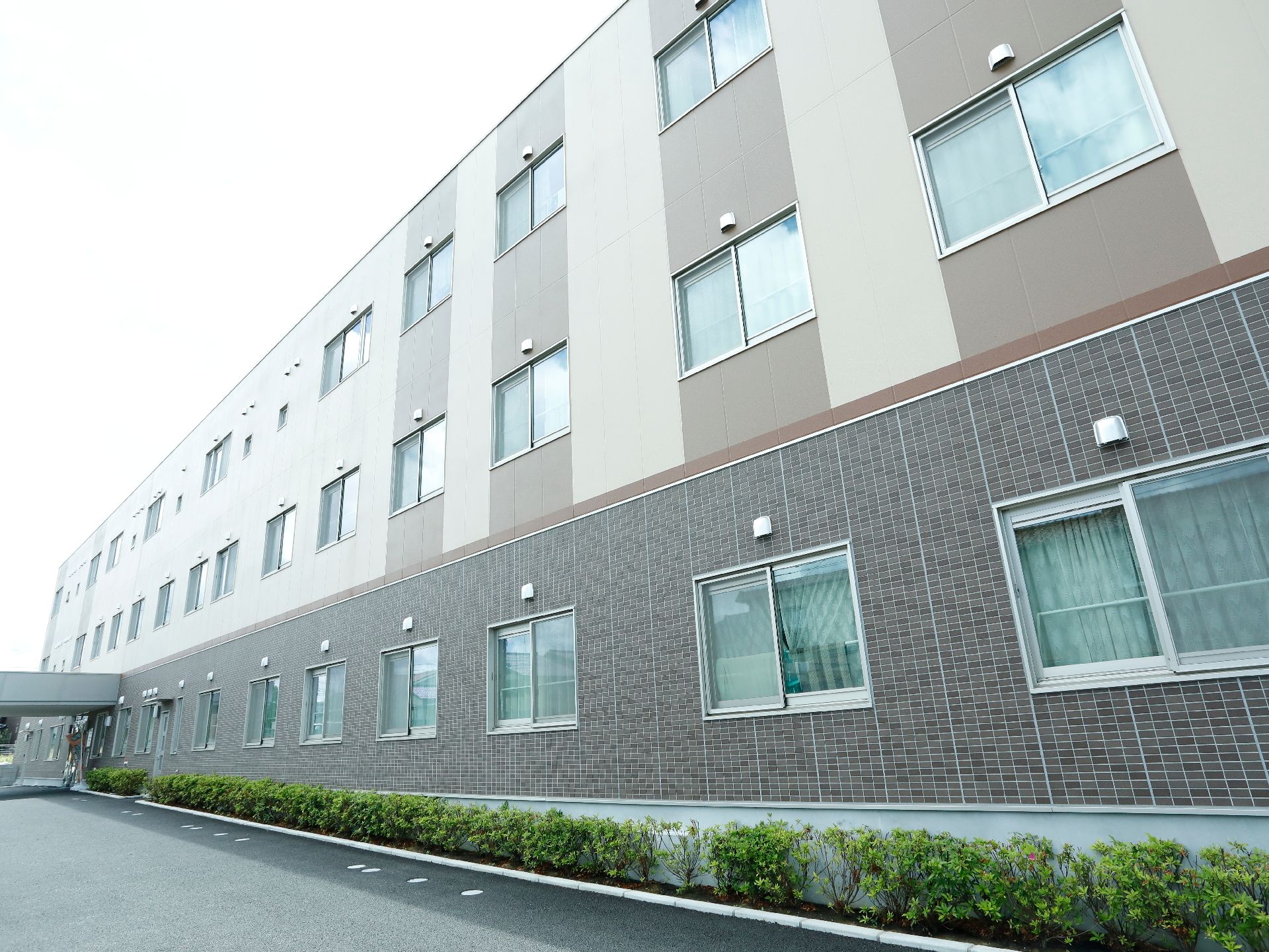 建物の前には植え込みがある。建物は1階部分がレンガ造りの様な壁になっており、それより上はクリーム色と茶色に塗られている。