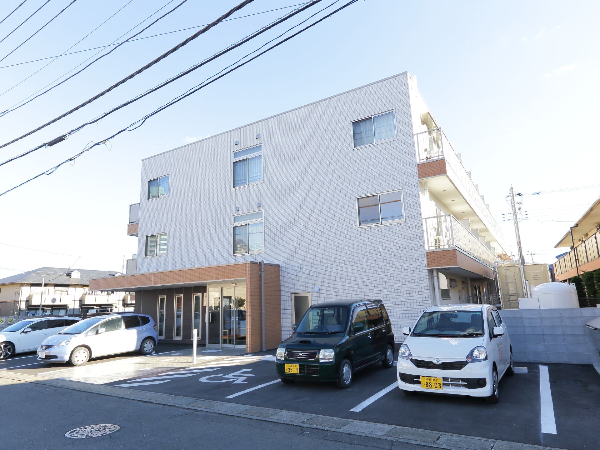 正面には玄関がある。玄関のそばには駐車場があり、障がい者用のスペースもある。建物の外壁の色は白色になっている。