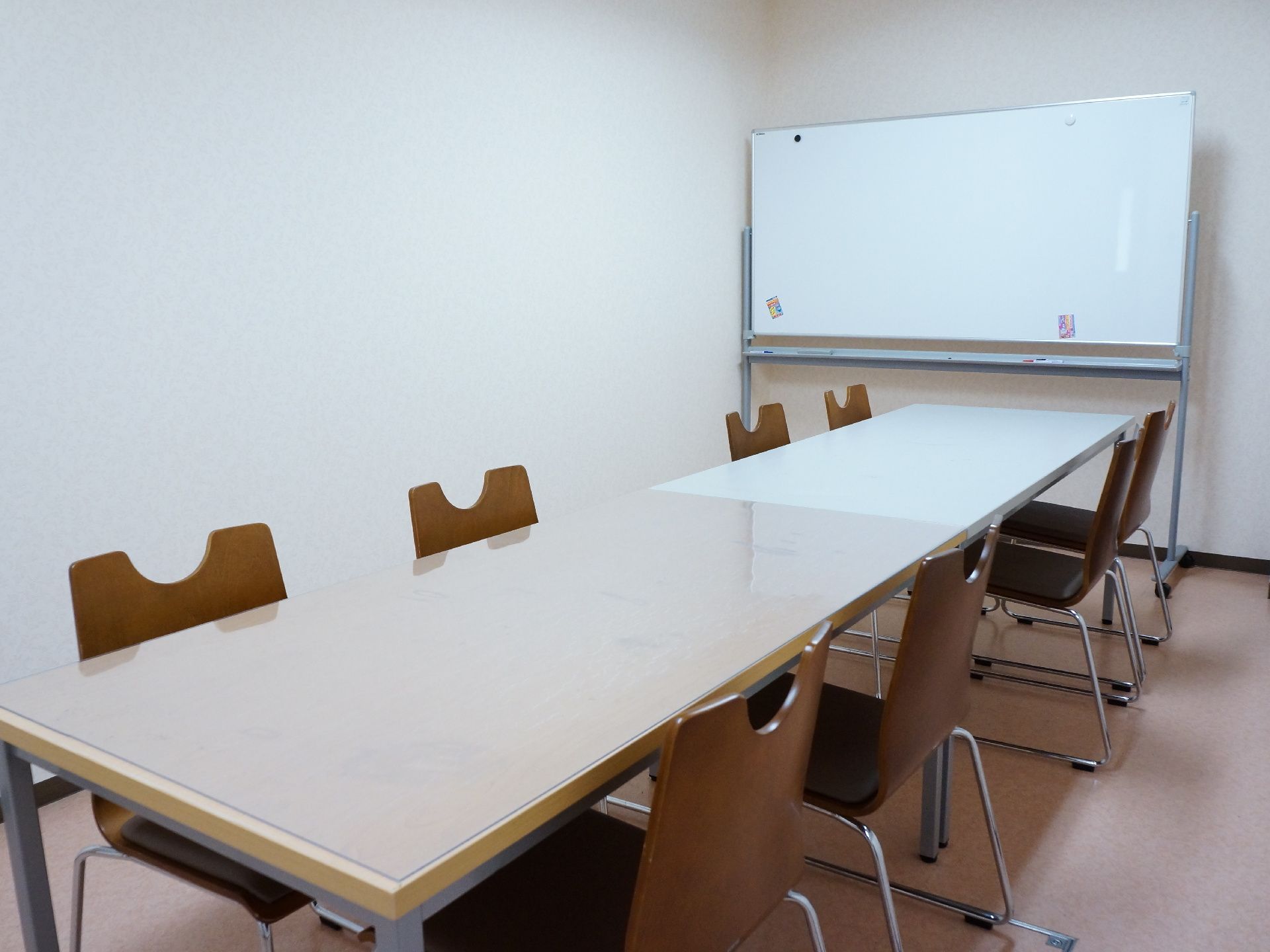 テーブルをはさんで、四脚ずつ椅子が向かい合わせに設置されている。奥にはホワイトボードが置かれている。