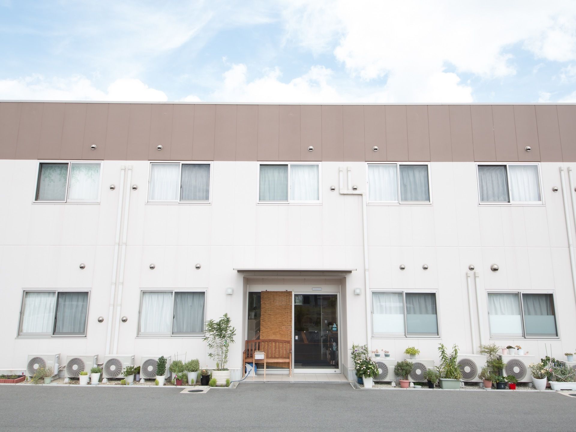 明るいホワイトの外壁が印象的な、清潔感のある佇まいの建物である。建物の外壁の上部は、淡い茶色になっている。