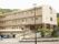 ピンクが基調となった３階建ての施設。壁には大きく施設名が描かれている。手前にある駐車スペースに車が何台も停まっている。