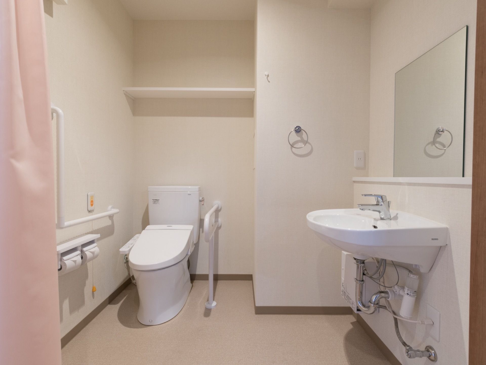 広い空間が確保されているトイレ洗面スペースである。左側の壁にはペーパーホルダーが二つあり、その上にコールボタンが付いている。