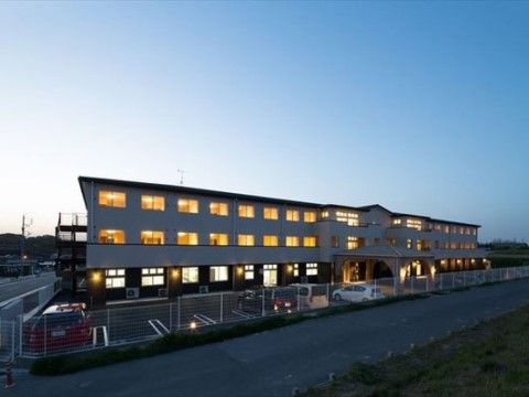 ３階建ての建物は、夜になるとオレンジがかったライトが灯る。前面には駐車場があり、白い網の柵で囲まれている。