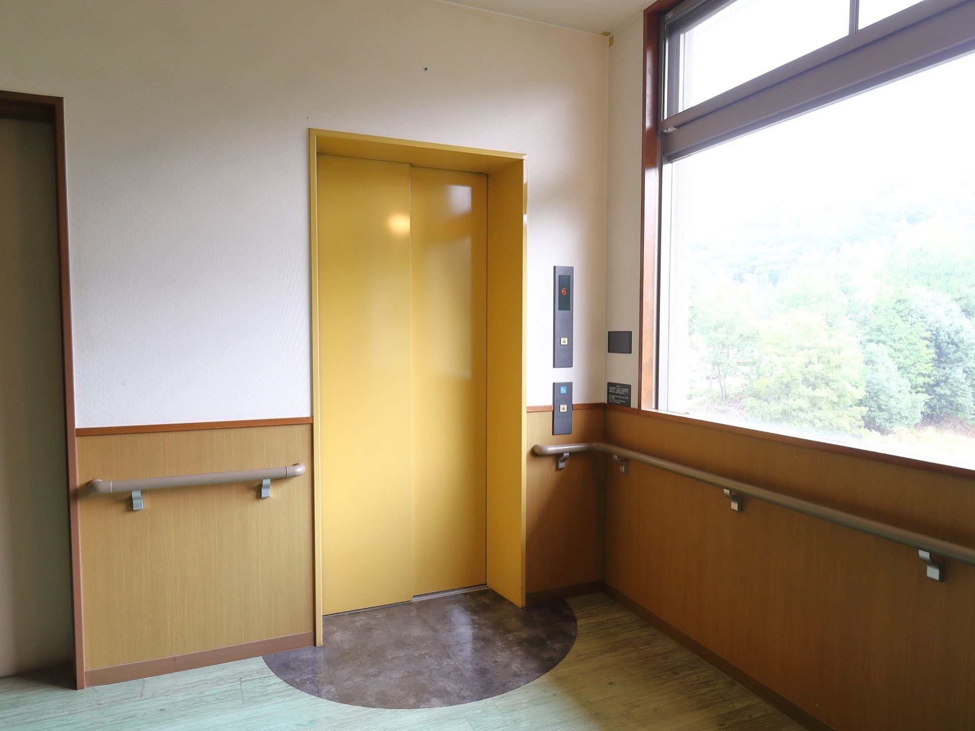 黄色い扉のエレベーターが設置されている。扉のすぐそばまで手すりが取付られている。車イスの方用に低いところにボタンがある。