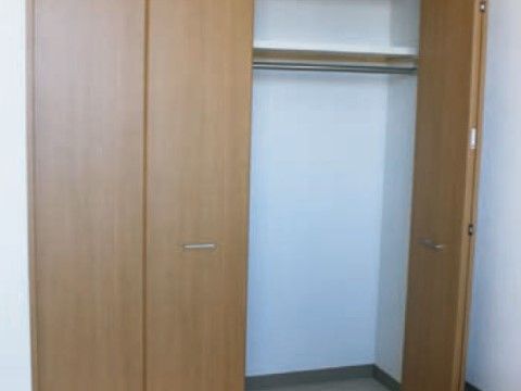 白い壁に設置された収納力のある大きなクローゼットである。扉は木目調の両開きとなっており、銀色の取っ手が付いている。