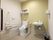 広々としたスペースに洋式トイレと洗面台を設置している。壁には複数の手すりやナースコールのほか、小物用の棚も完備している。